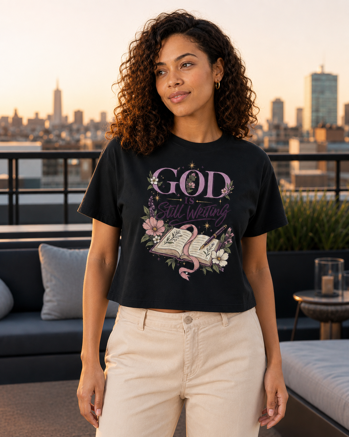 Woman wearing the God Is Still Writing tee outdoors at golden hour
