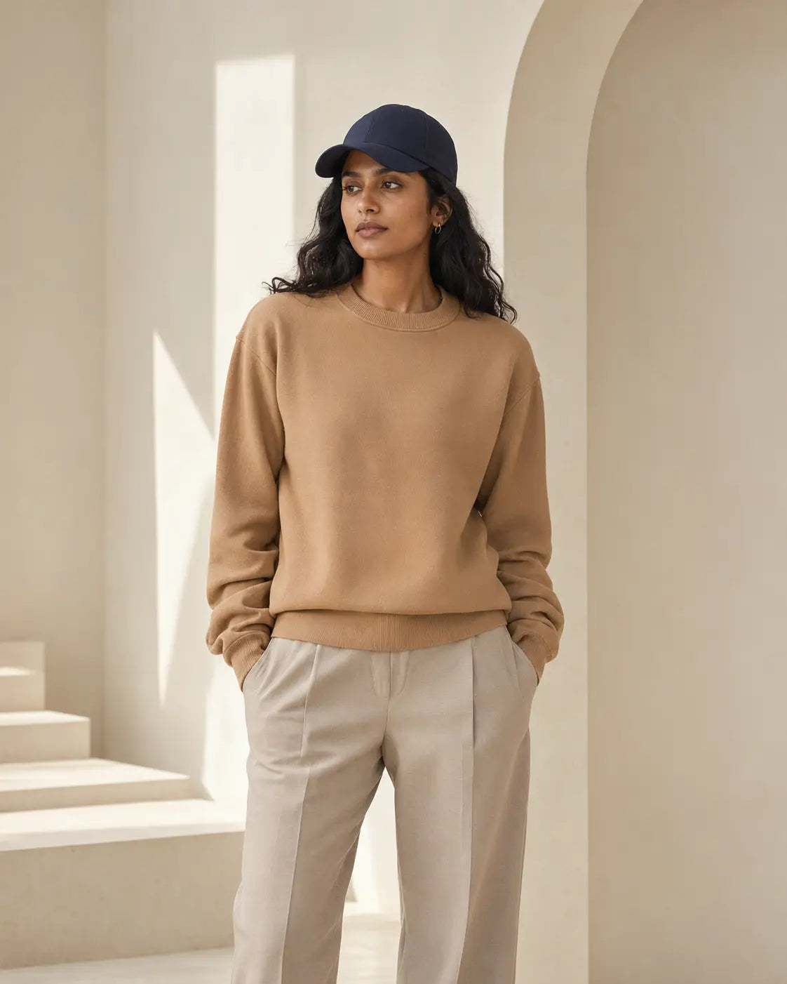 Woman wearing a camel crewneck and navy cap
